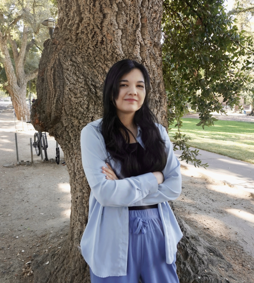 A woman with her arms crossed, long hair, in front of a tree 