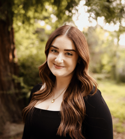 A woman smiling at the camera with a tree in the background