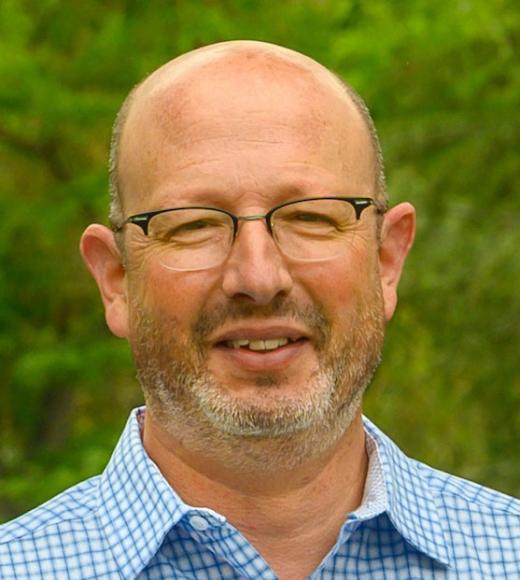 A portrait of a man with glasses wearing a blue collared shirt