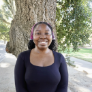 A woman in a black top standing in front of a tree