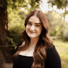 A woman smiling at the camera with a tree in the background