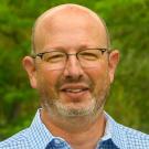 A portrait of a man with glasses wearing a blue collared shirt